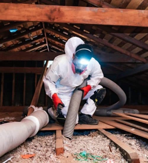 Professional insulation crew member in protective gear working in an attic
